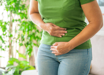 Person in a green shirt holds their stomach, indicating abdominal pain or discomfort.